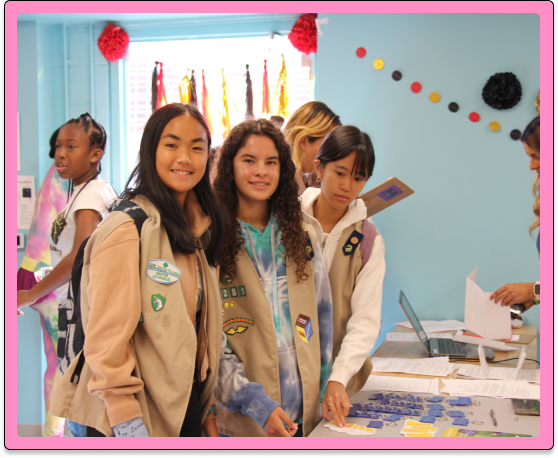Four young girl scouts smiling at the camera in their tan-colored vests.